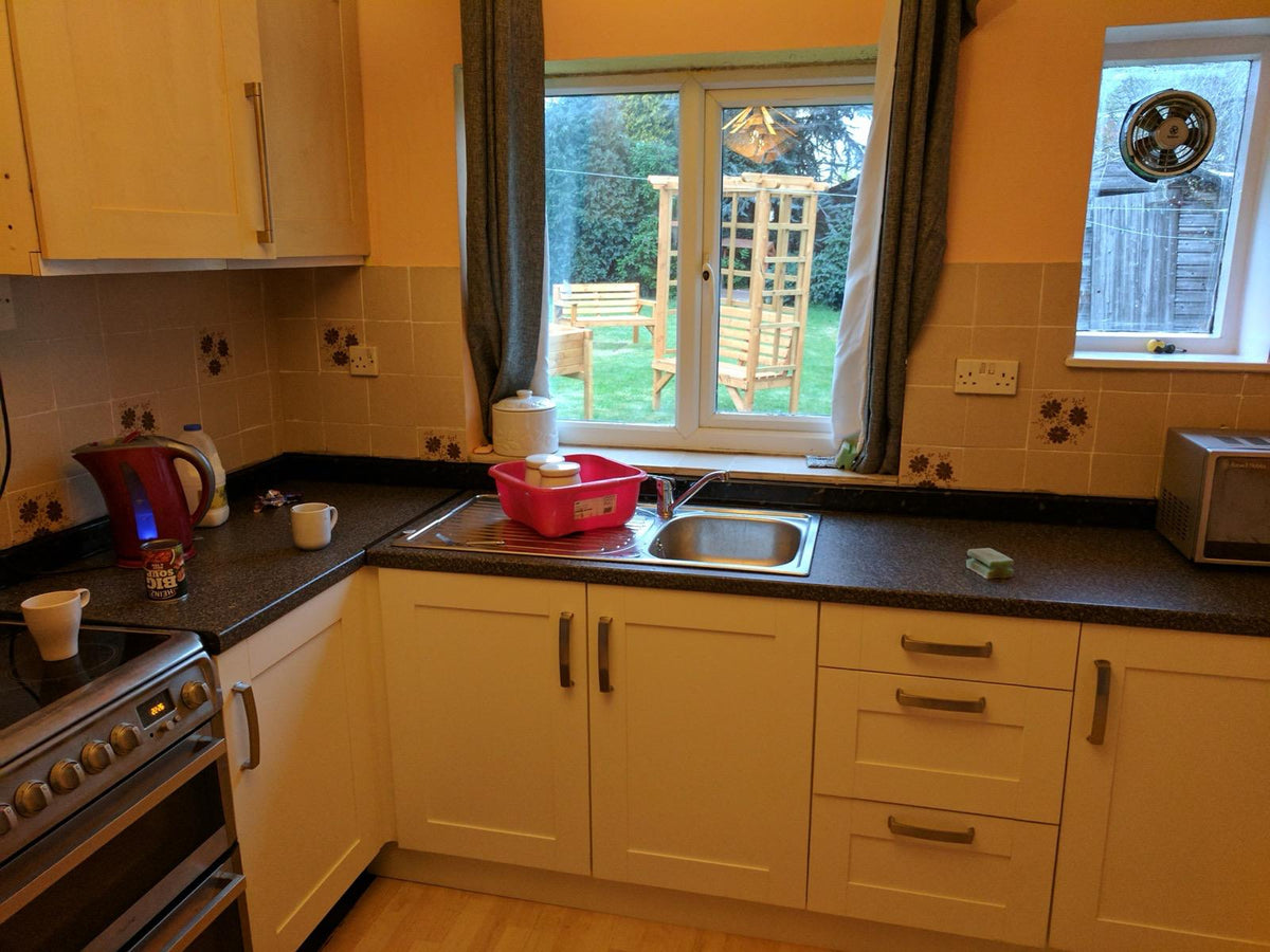 A family kitchen with cream cupboards, a dark worktop and a sink under a window looking onto a garden.